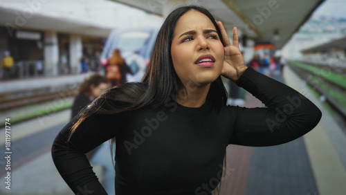 Foto Woman listening at a bustling train station platform outdoors, showcasing young hispanic presence amid modern rail travel with curiosity