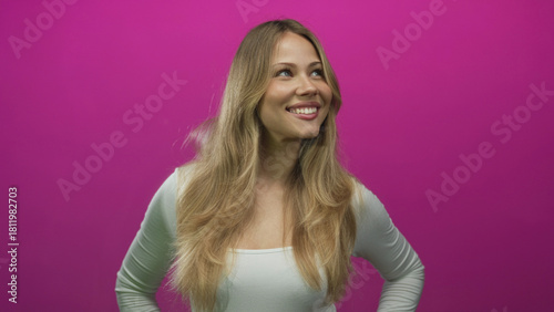 Woman stands with hands on hips in a photo studio setting while smiling broadly and looking upward; confidence joy optimism positivity.