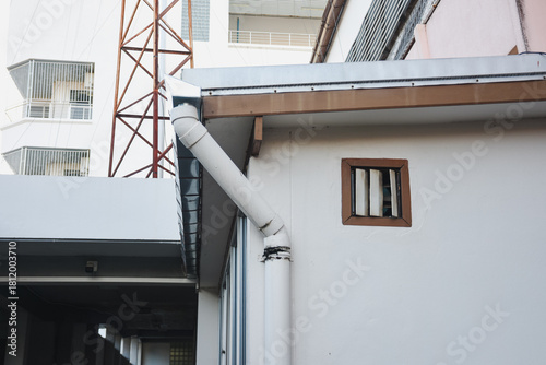 Fototapeta Naklejka Na Ścianę i Meble -  White drainpipe on building, with a small barred window.