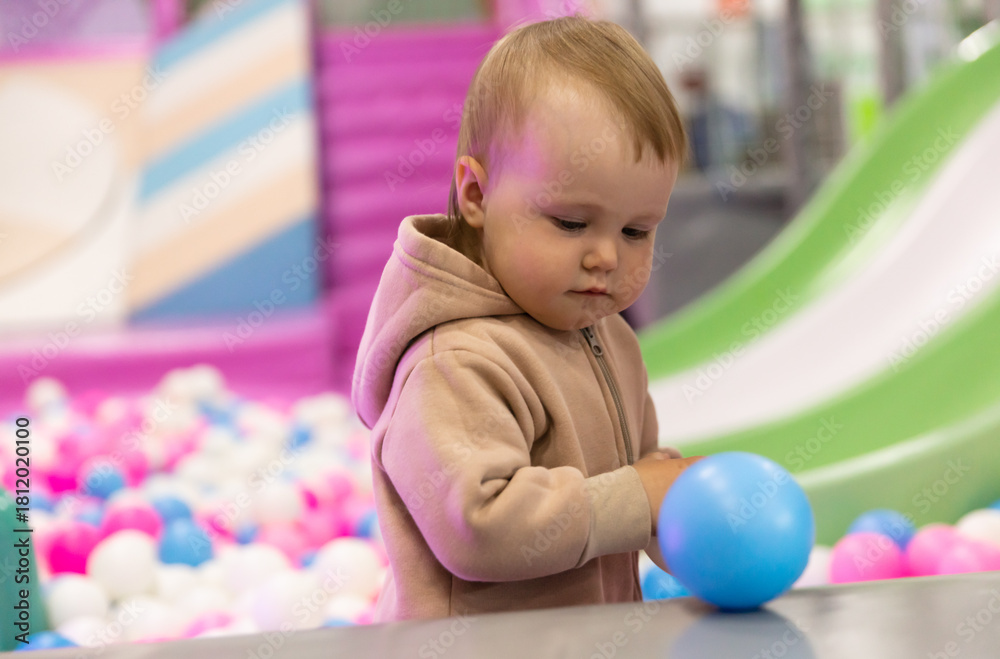 Fototapeta premium Cute little baby plays with balls in a dry pool at a children's entertainment center