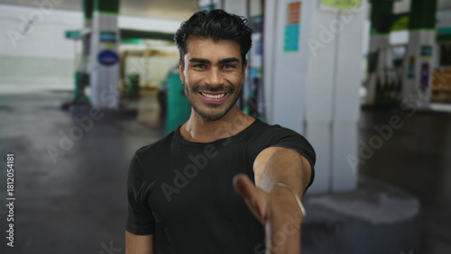 Hispanic man smiles and extends hand for handshake at urban petrol station on street; trust connection.