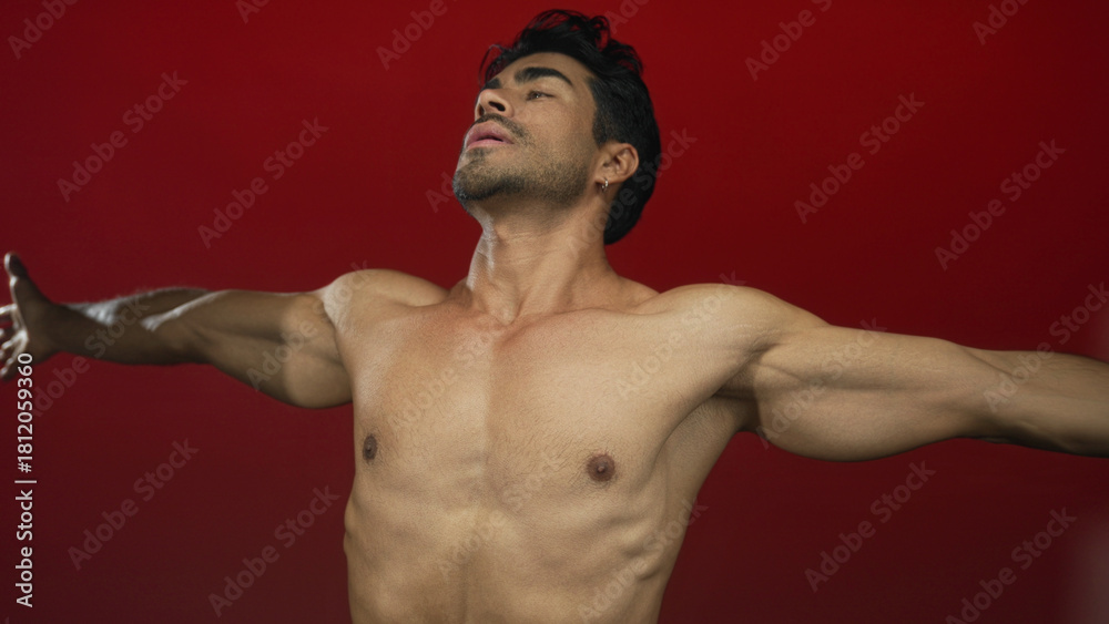 Obraz premium Man with bare chest and outstretched arms in a red studio setting showing muscular torso and shoulders; serenity.
