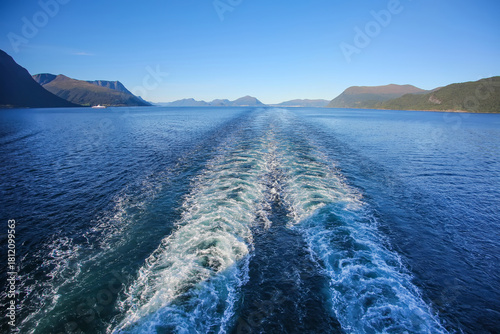 Wake of the cruise ship while scenic cruising out of the fjord. Beautiful landscape with mountains along the water on a calm summer day, Norwegian fjords, Norway.
