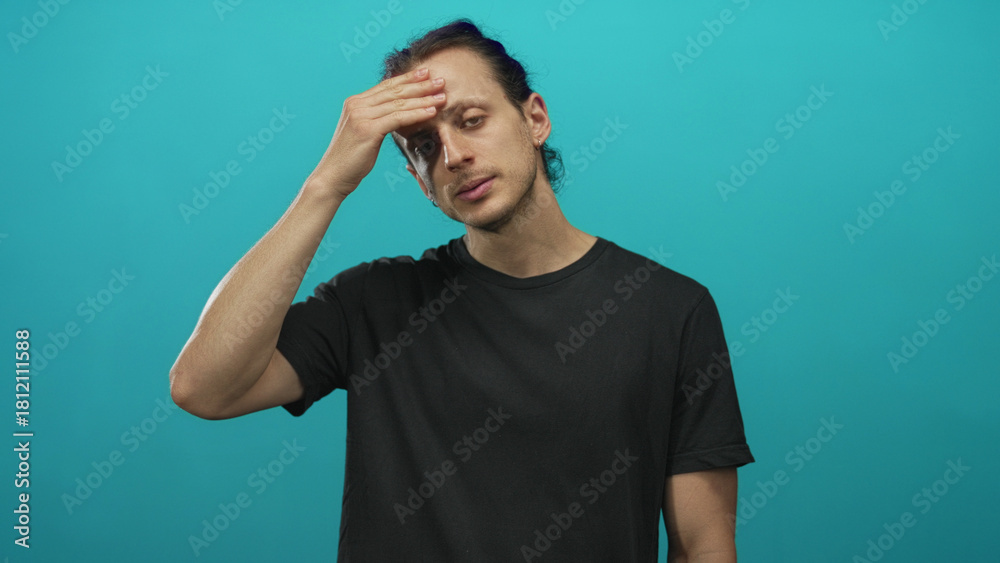 Fototapeta premium Young hispanic man with long hair, hand on forehead and eyes closed against a teal studio backdrop; fatigue reflection.