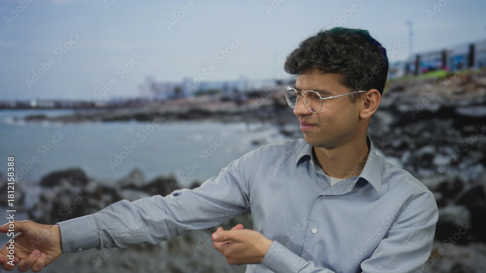 Fototapeta premium Man pointing finger at seaside shoreline while looking toward the horizon wearing a blue shirt; serenity reflection calm tranquility.
