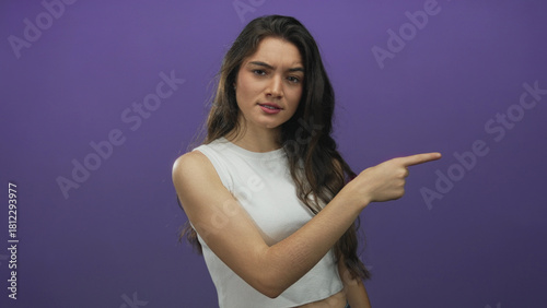 Fotografie Young hispanic woman with furrowed brow pointing finger toward viewer in purple studio; rebuke anger