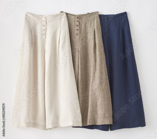 Three pairs of linen culottes in neutral tones hang on white background
