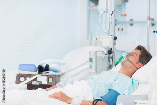 фотографія Male patient lying supine on hospital bed receiving oxygen mask and IV pump, cop