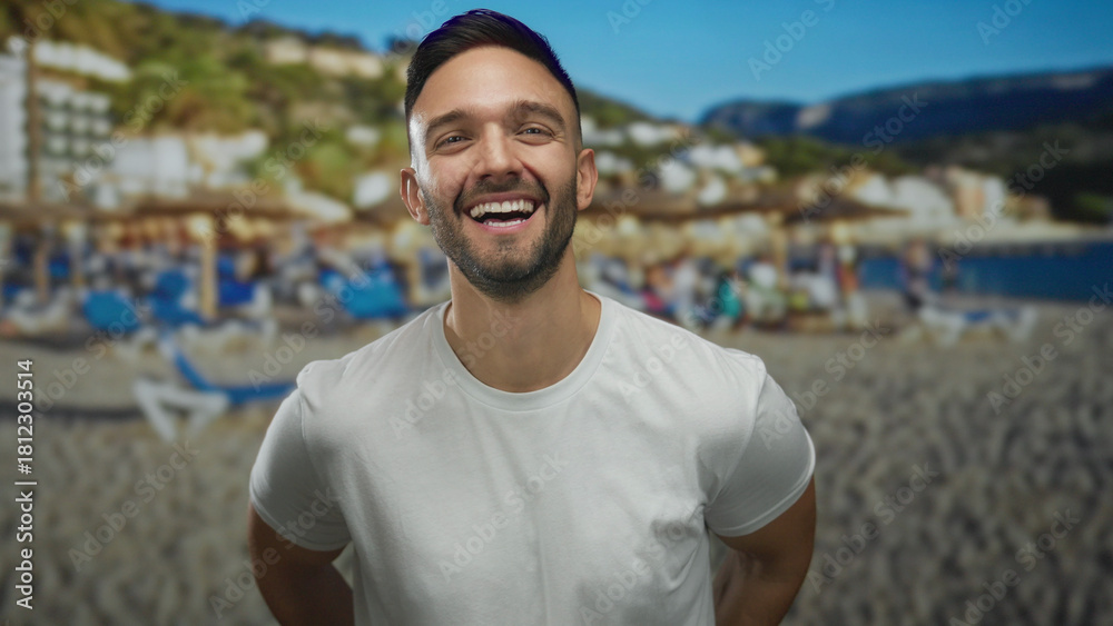 Fototapeta premium Young hispanic man smiling at the beach with sun umbrellas and scenic coastline backdrop, capturing the essence of a relaxed seaside vacation day.