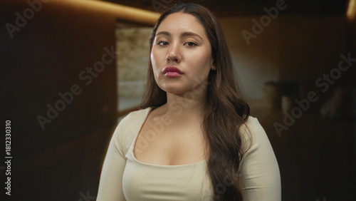 Young woman with long brown hair and subtle neutral expression looking at camera in a studio; serenity. Free Download Young woman with long brown hair and subtle neutral expression looking at camera in a studio; serenity. - GFXLoad