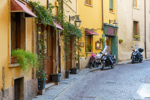 Fototapeta Naklejka Na Ścianę i Meble -  A street with a few shops and a couple of motorcycles in Verona Italy. The shops are yellow and the motorcycles are black