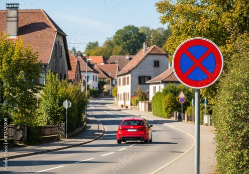 Fototapeta Naklejka Na Ścianę i Meble -  Red car drives down a street with a no parking sign
