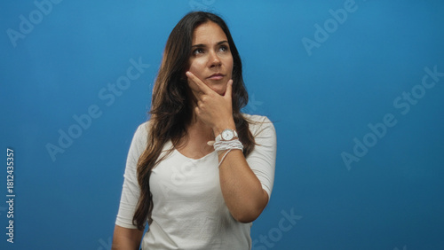 Fényképezés Woman with hand on chin and wristwatch visible in blue studio, half length portrait looking up in thinking pose; thoughtful reflection