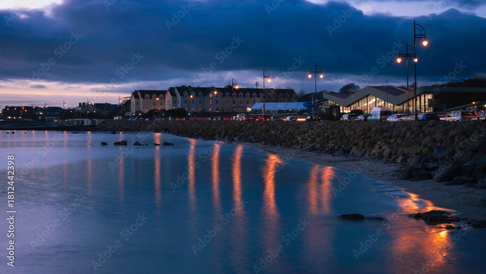 Obraz premium Salthill Promenade sunset seascape in Galway, Ireland, a romantic nightscape illuminated by street lights and buildings at the charming coastal village on the North Atlantic Ocean.