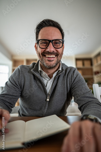 Smiling man wearing glasses writing in notebook at home