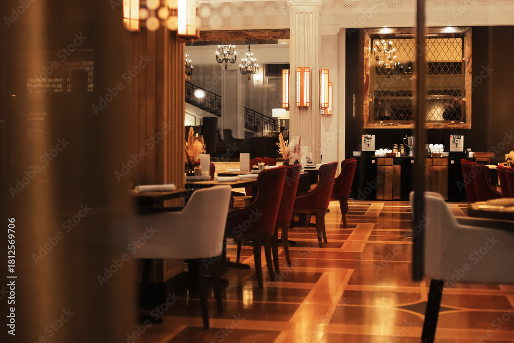 Obraz premium An elegant luxury restaurant dining room interior with plush red and white chairs, warm lighting, and glossy wood flooring.
