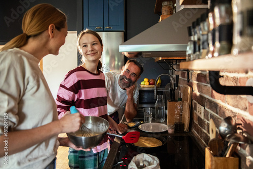 Cuadro en lienzo Adult parents and teen daughter smiling while cooking pancakes in home kitchen