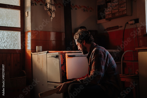 Cuadro en lienzo Despaired man sitting by wood stove in aged interior.