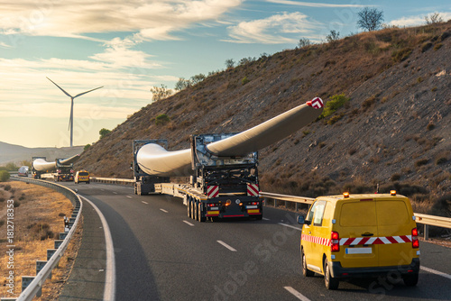 Oversized transport convoy carrying multiple wind turbine blades on the road with escort vehicles