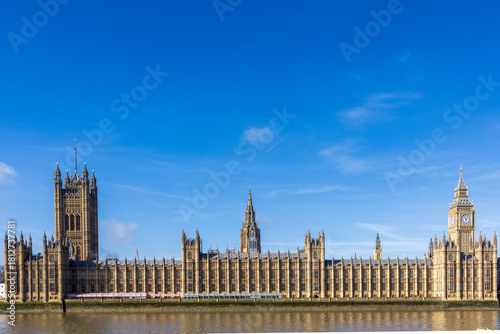 Houses of Parliament and Big Ben by the Thames under a clear blue sky.
