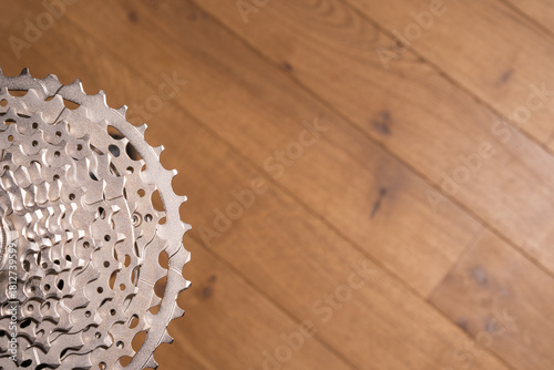 Close-up of a multi-sprocket bicycle cassette resting on wood flooring, showing gear progression and hub interface