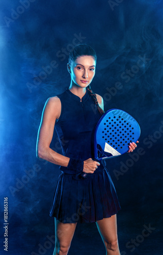 Sports portrait of active female player in motion holding padel racket under blue pink light in dark background