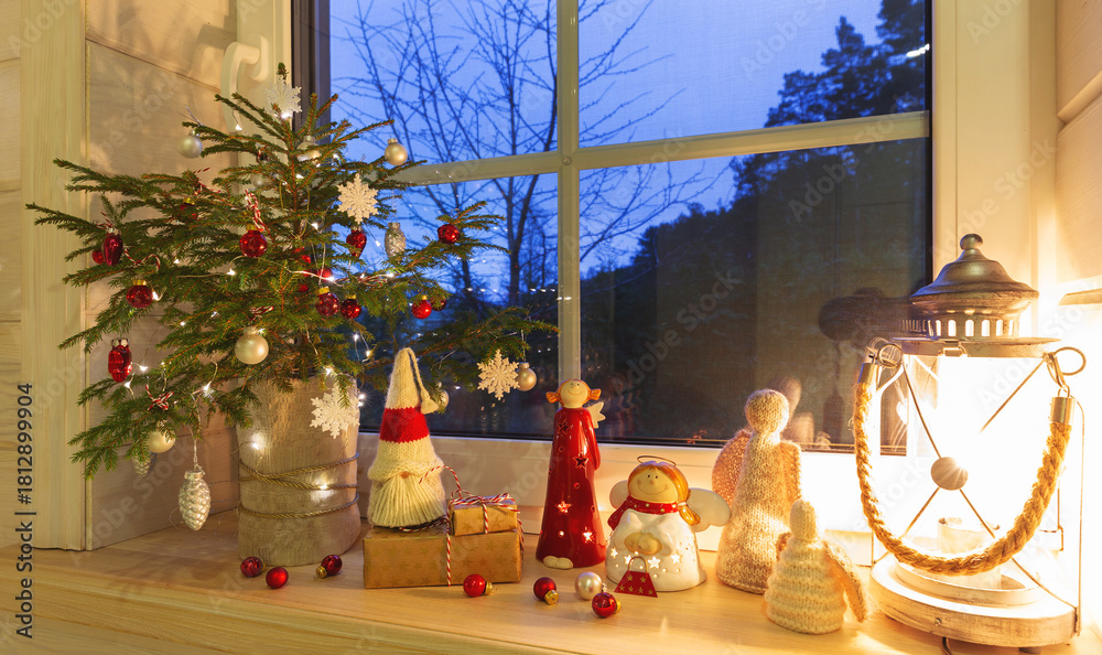 Naklejka premium Cozy Christmas window scene with small tree, glowing lights, handmade angels, festive decor, warm evening mood, holiday inspiration, winter home atmosphere, beautiful seasonal background for