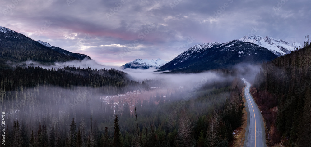 Naklejka premium Misty Valley Road Through Snowy Mountain Range in BC, Canada at Sunset