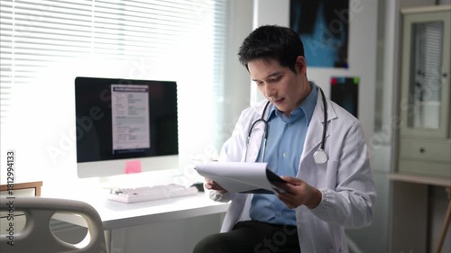 Wallpaper Mural A doctor is sitting at a desk with a computer and a clipboard. He is looking at the computer screen and he is focused on the task at hand Torontodigital.ca