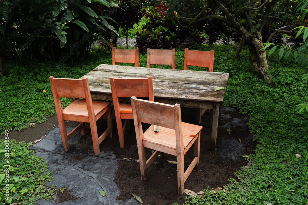 Obraz premium Rustic Wooden Table and Chairs Surrounded by Lush Greenery