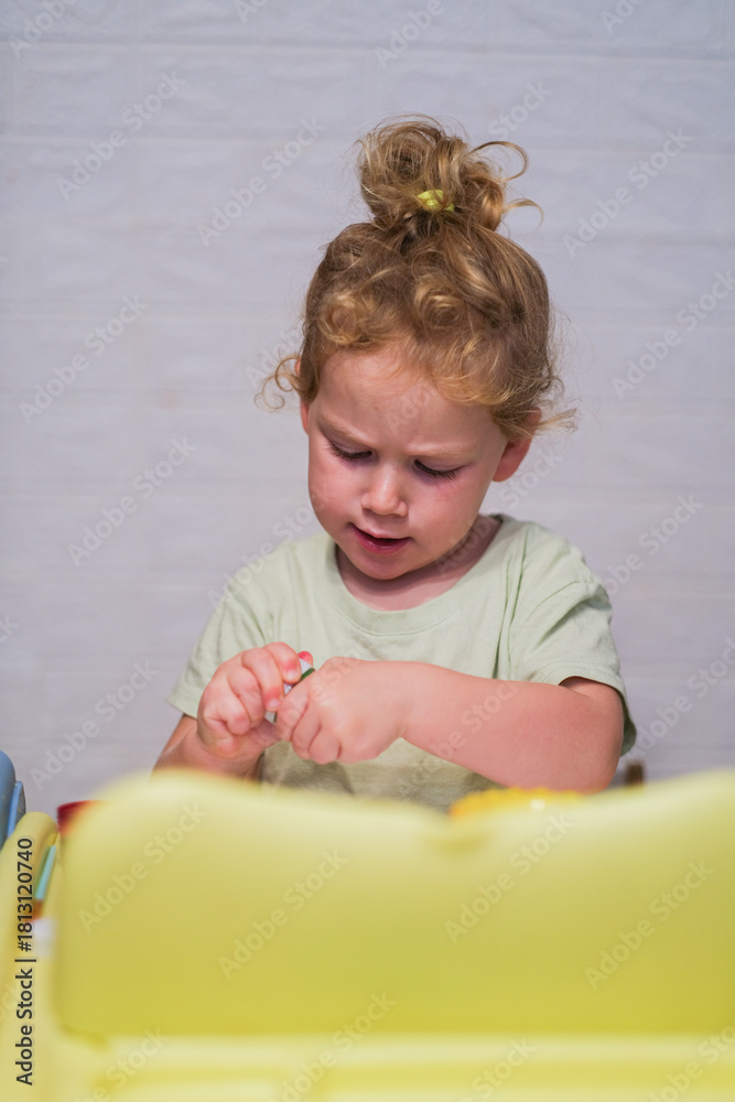Fototapeta premium Young caucasian child with curly fair hair playing with toy. Kid with concentration at home. Learning, development, childhood concept.