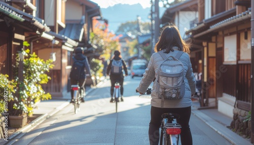 Three people ride bicycles on a street lined with traditional Japanese buildings on a sunny day.