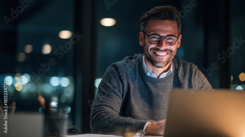 Portrait of smiling young businessman doing online research over laptop while sitting at desk in office