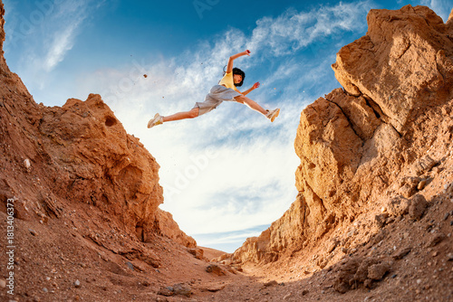 Young hiker woman girl tourist makes long jump across small gorge against blue sky