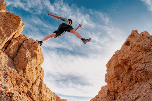 Man hiker jumps or make big step over small desert gap against blue sky