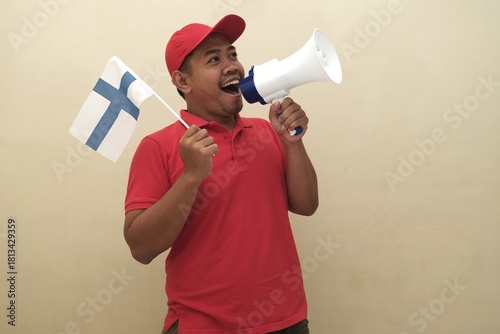Southeast Asian man holding Finland flag and megaphone, promoting visa, scholarship, or study abroad opportunities in Italy; isolated with copy space for advertisement.