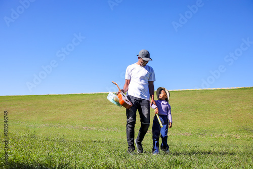 Father and His Daughter Walk Across a Sunlit Green Hill, Holding Hands and Carrying Their Picnic Gear
