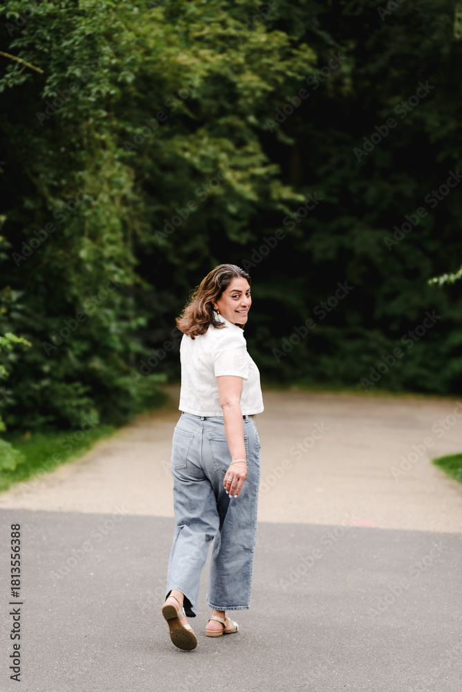 Obraz premium Woman looks back playfully while walking toward a shaded forest path.