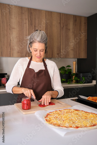 Senior woman cutting vegetables for a delicious homemade pizza in a modern kitchen