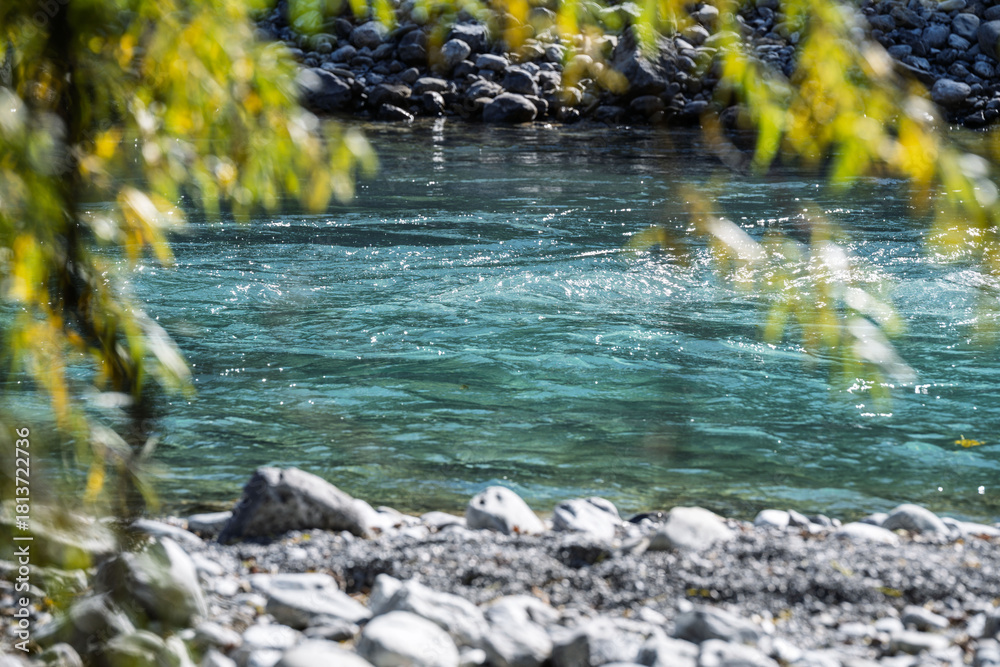 Fototapeta premium Turquoise river flowing between rocks on a sunny autumn day, surrounded by warm fall colors and clear water, showcasing a serene alpine landscape