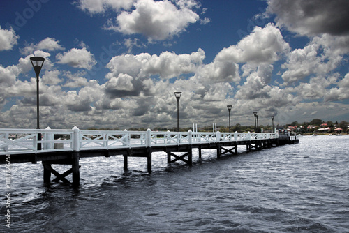 A wooden jetty extends out across a lake below dense fluffy storm clouds