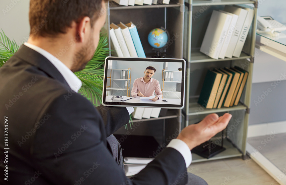 Fototapeta premium Businessman on tablet during video call. Remote meeting in modern office shows online interview, webinar, clear communication, and expert consulting. Remote teamwork and technology concept.