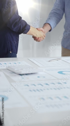 Businesspeople shaking hands over a conference table, finalizing a deal with financial documents and digital tools. Handshake concept