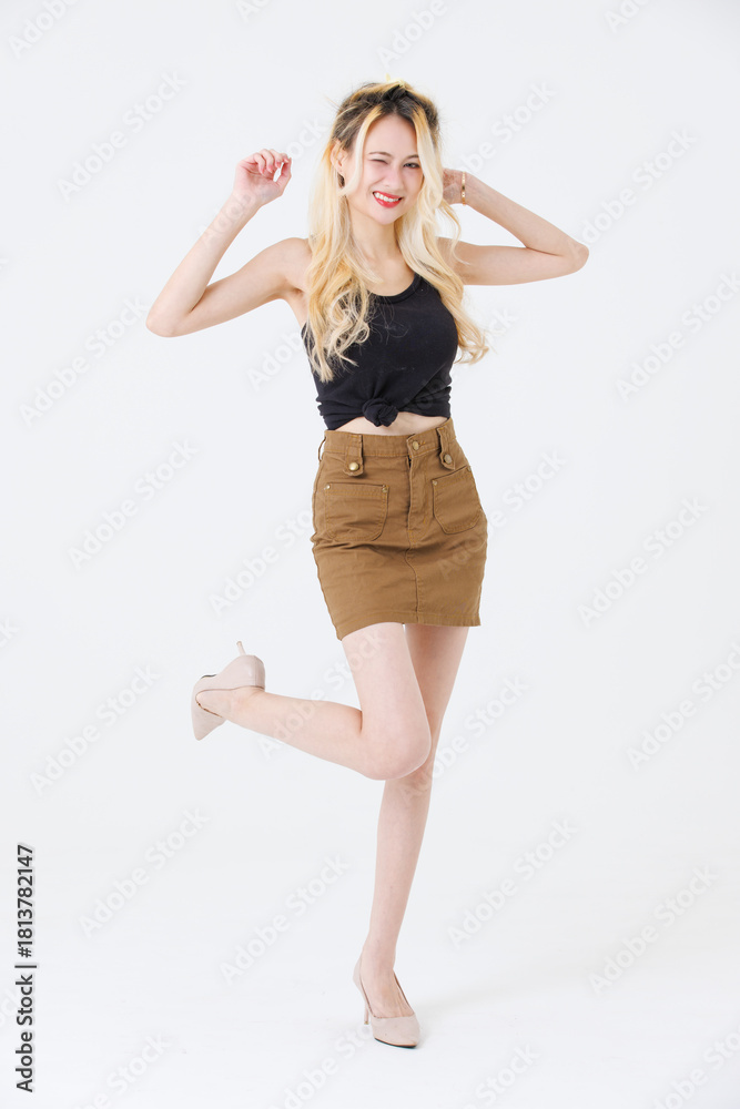 Fototapeta premium Asian beauty attractive woman blonde long hair stand wear black sleeveless top brown short skirt on white background studio portrait fashion street outfit trendy style pose look at camera full length.