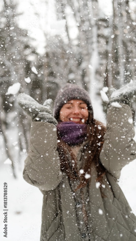 Fototapeta premium A beautiful young woman in winter clothes is happily spending her free time in a snowy forest. She enjoys the first snow. Active winter recreation.