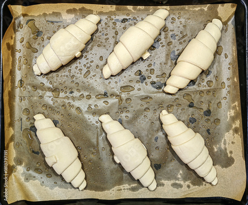Fresh uncooked homemade croissants placed on parchment paper on a baking tray, ready for the oven. Top view, clean food photography