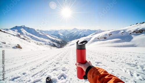 Person holding a red water bottle against snowy mountains