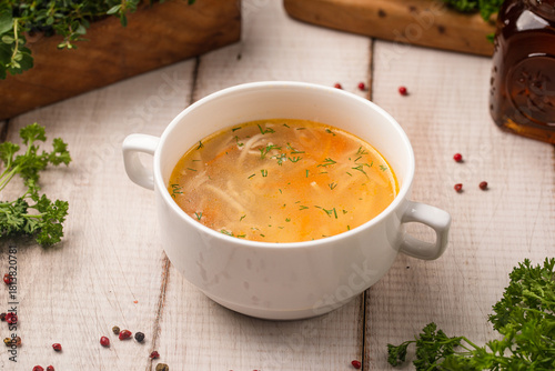 Classic chicken noodle soup with herbs served in a white bowl on rustic wooden table