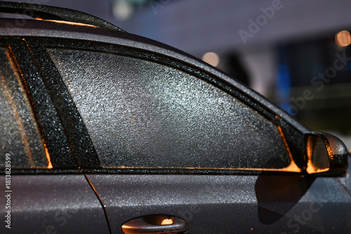 Close-up of frosted car window coated with ice from freezing rain captured under dark night view. Frozen glass effect during the cold winter night. Icy windshield, selective focus