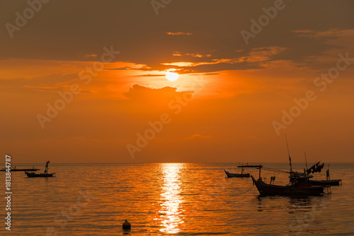 Fishing boats floating on calm sea during vibrant orange sunset with dock in foreground and golden reflections on water surface